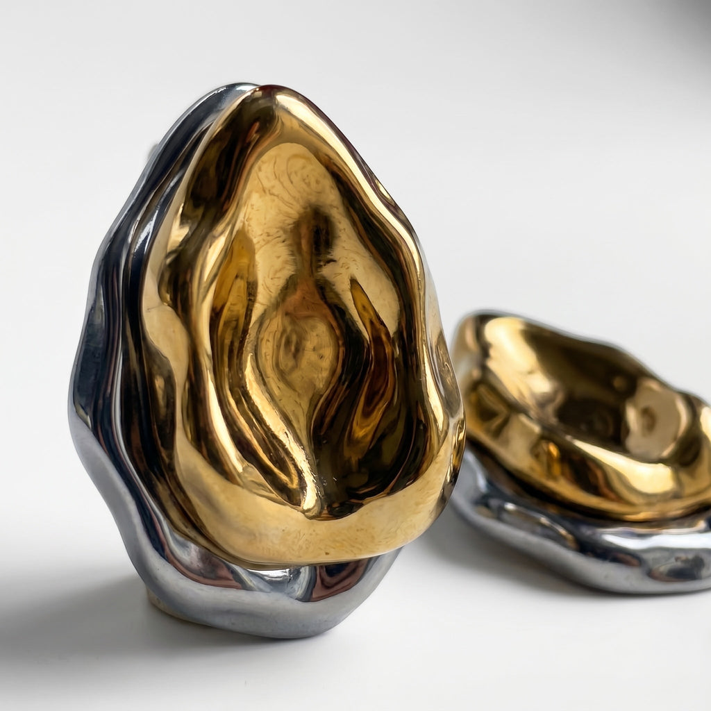 TALI abstract sculptural statement earrings featuring a fluid, molten metal design in polished gold and silver tones.